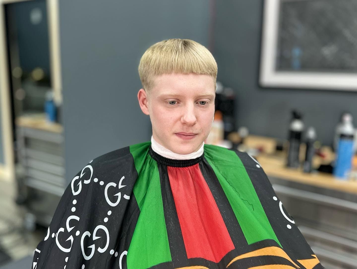 Person seated in a barber chair wearing a black, green, red, and yellow cape in a salon