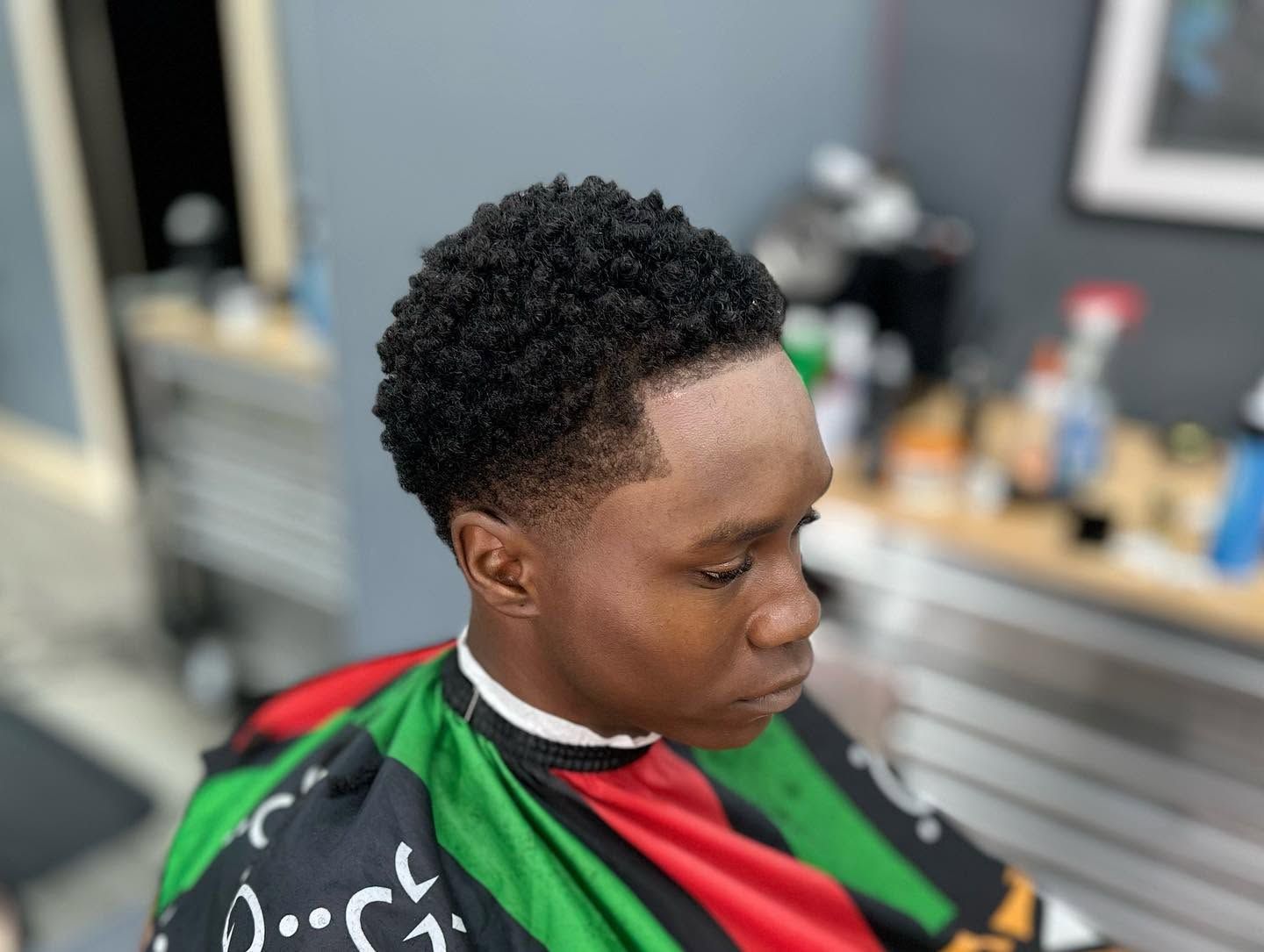 Person in a red, green, and black barber cape looking down in a salon chair