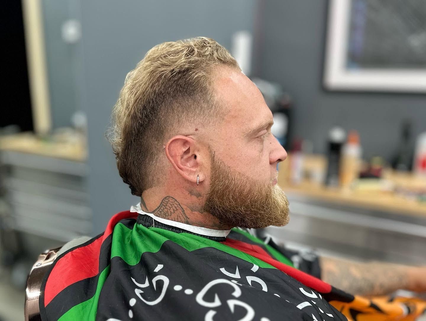 Side profile of a bearded man in a barber cape sitting in a barbershop chair