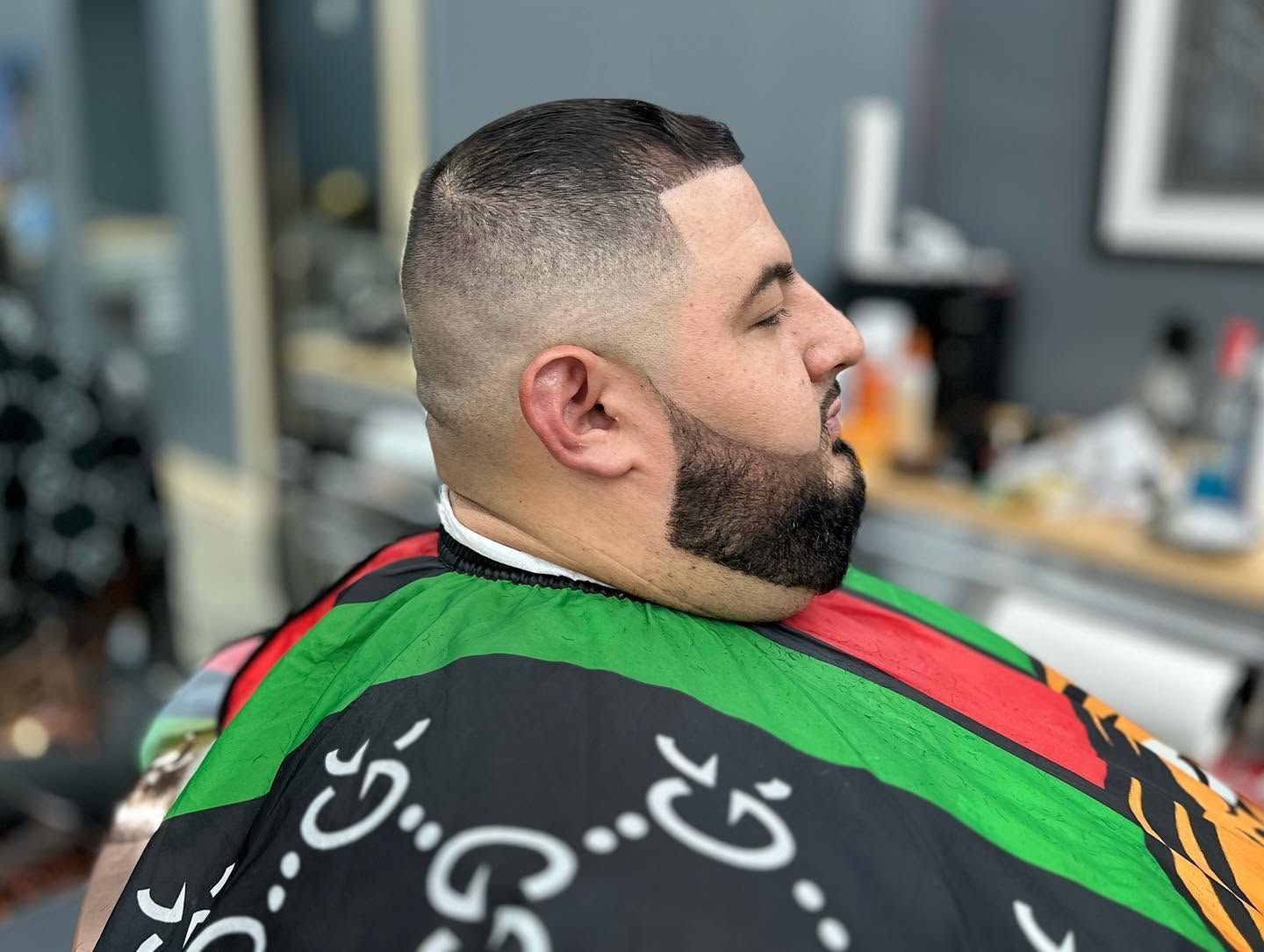 Man getting a fresh haircut in a barbershop, with a fade and patterned barber cape.