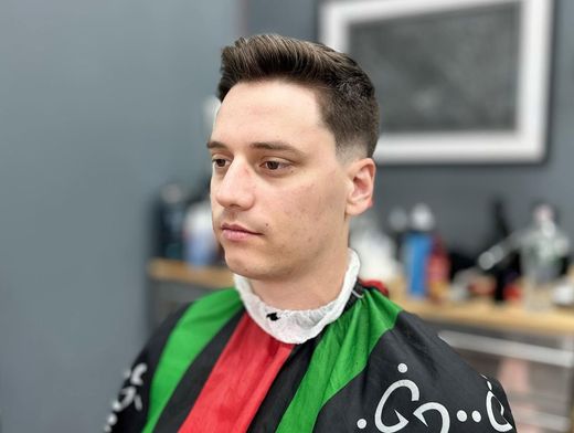 Person in a barber cape with green and red stripes, seated in a salon with a neutral expression.