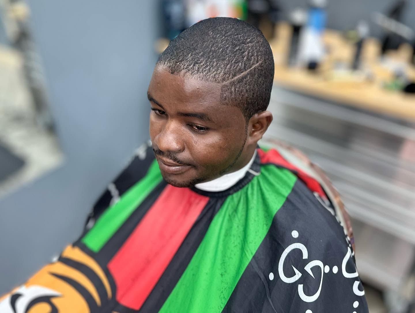 Man getting a haircut, wearing a red, green, and black barber cape.