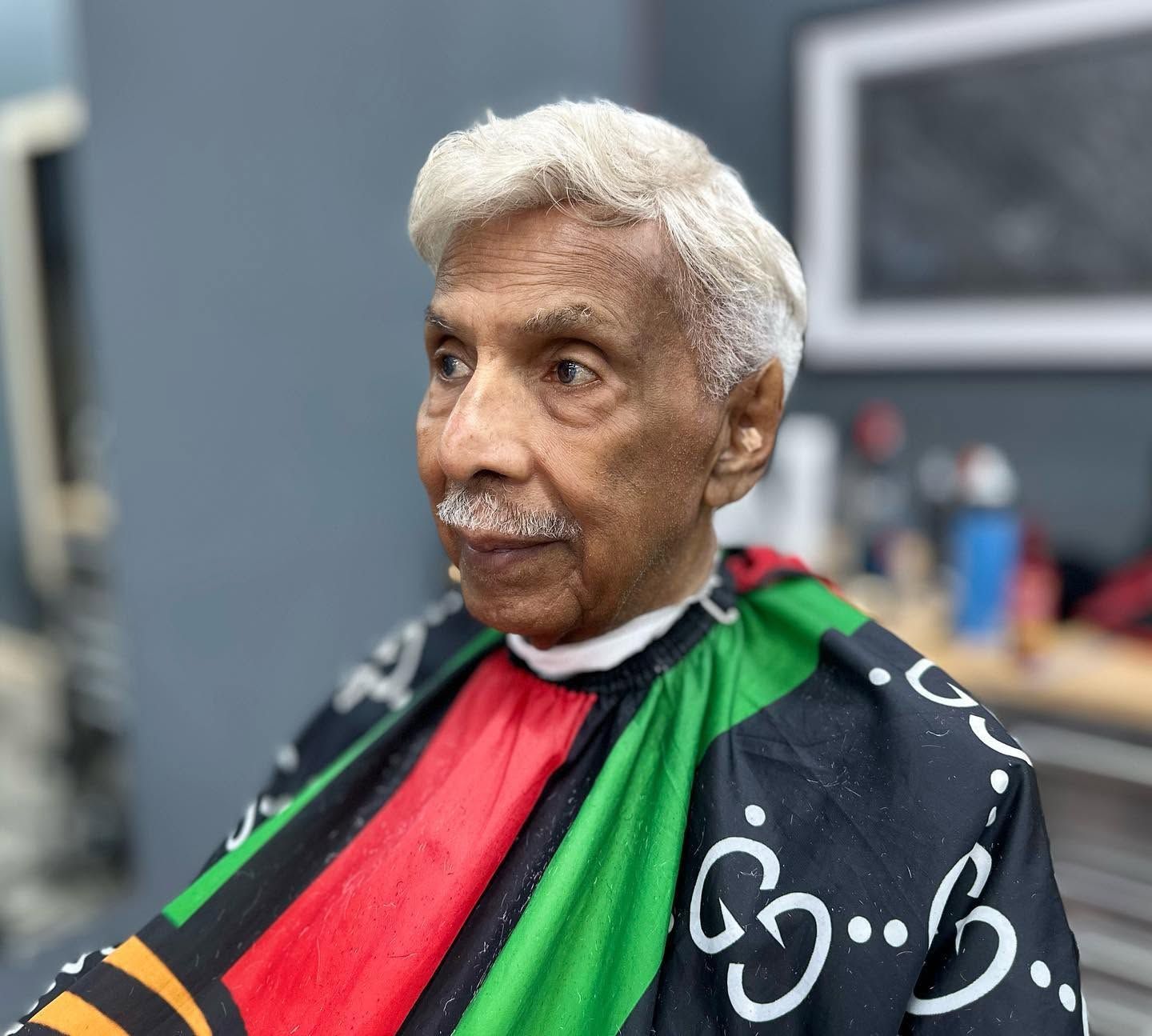 Portrait of a person in a black cape with red and green stripes, seated indoors against a blurred background