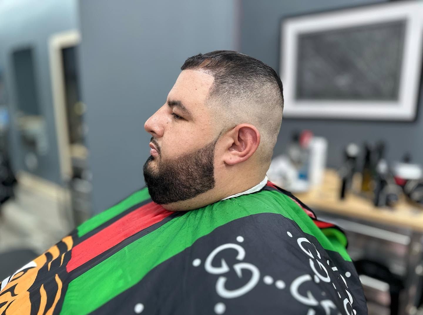 Man seated in a barber chair wearing a green and black cape during a haircut