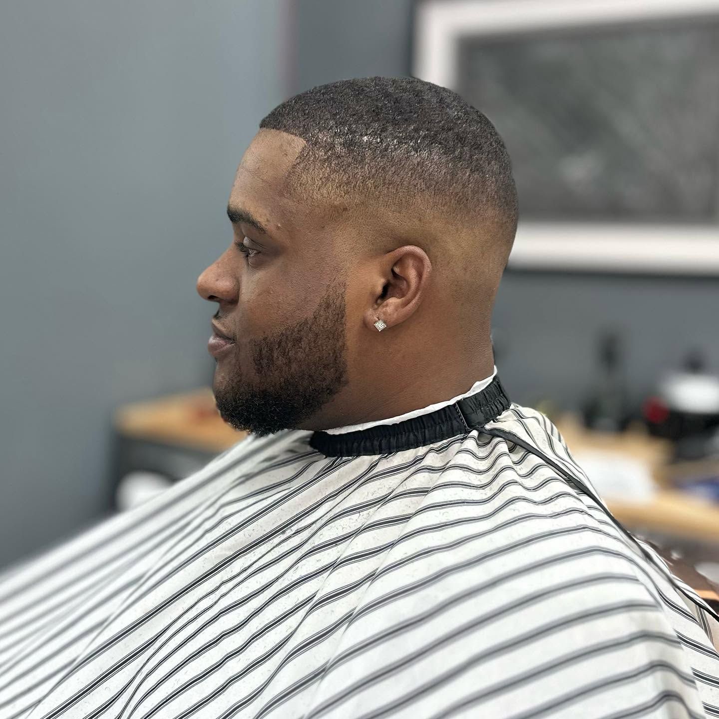 Man getting a close fade haircut in a barber chair, wearing a black-and-white striped cape.