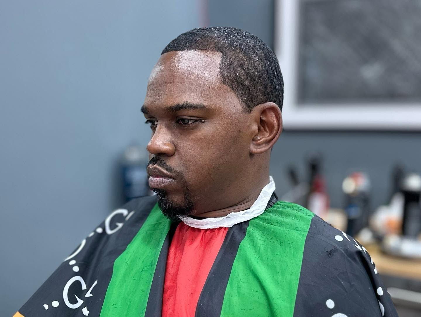 Man with a black, green, and red barber cape looking down in a barbershop chair