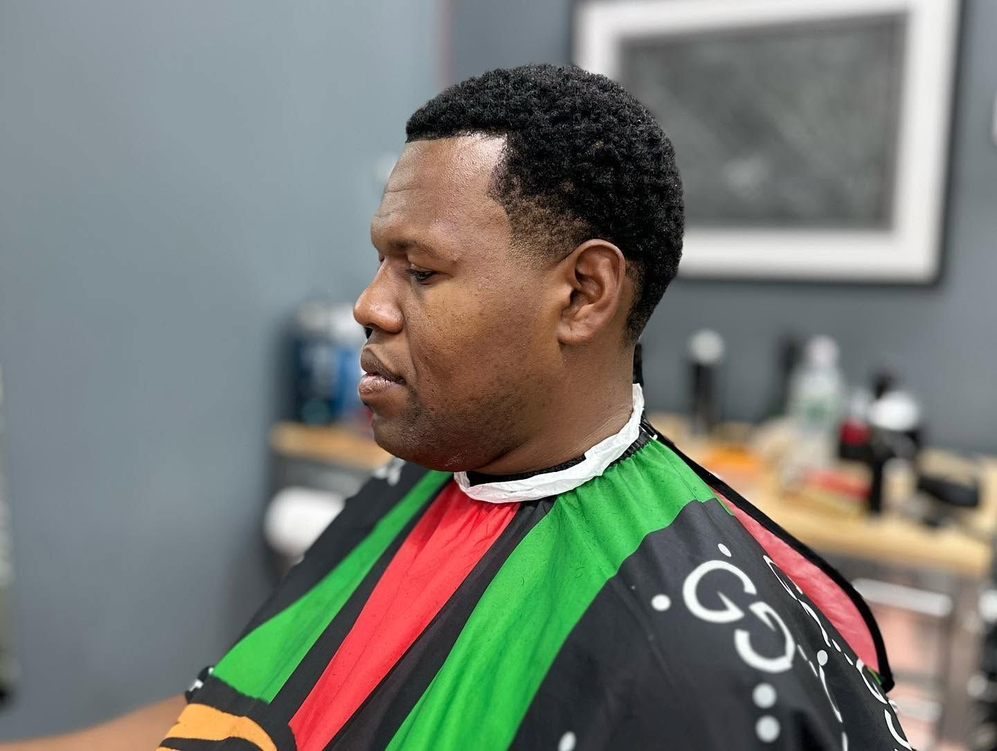 Person in a barber chair wearing a green, red, and black cape during a haircut.