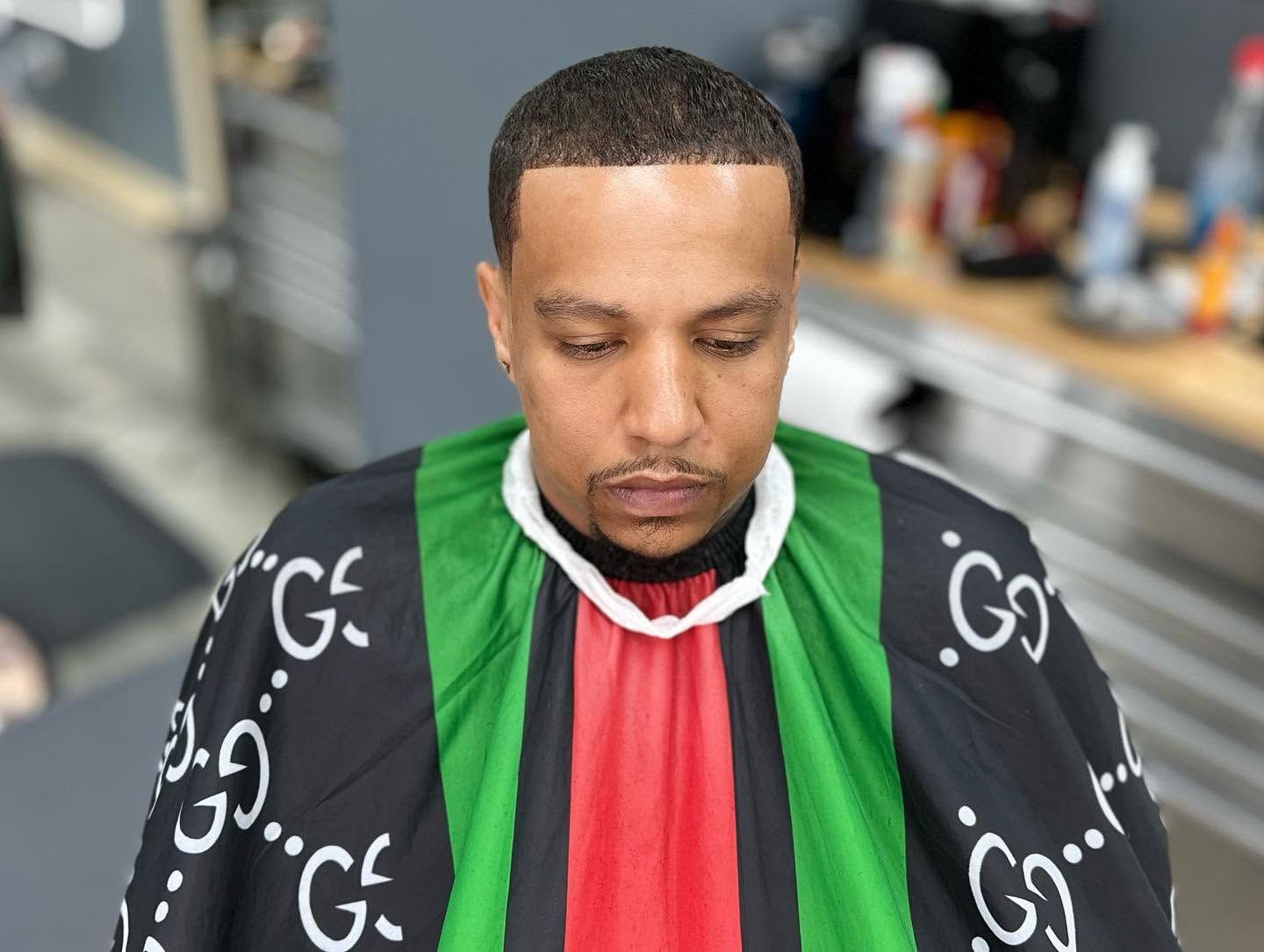 Man in a green, black, and red barber cape looking down in a barbershop seat