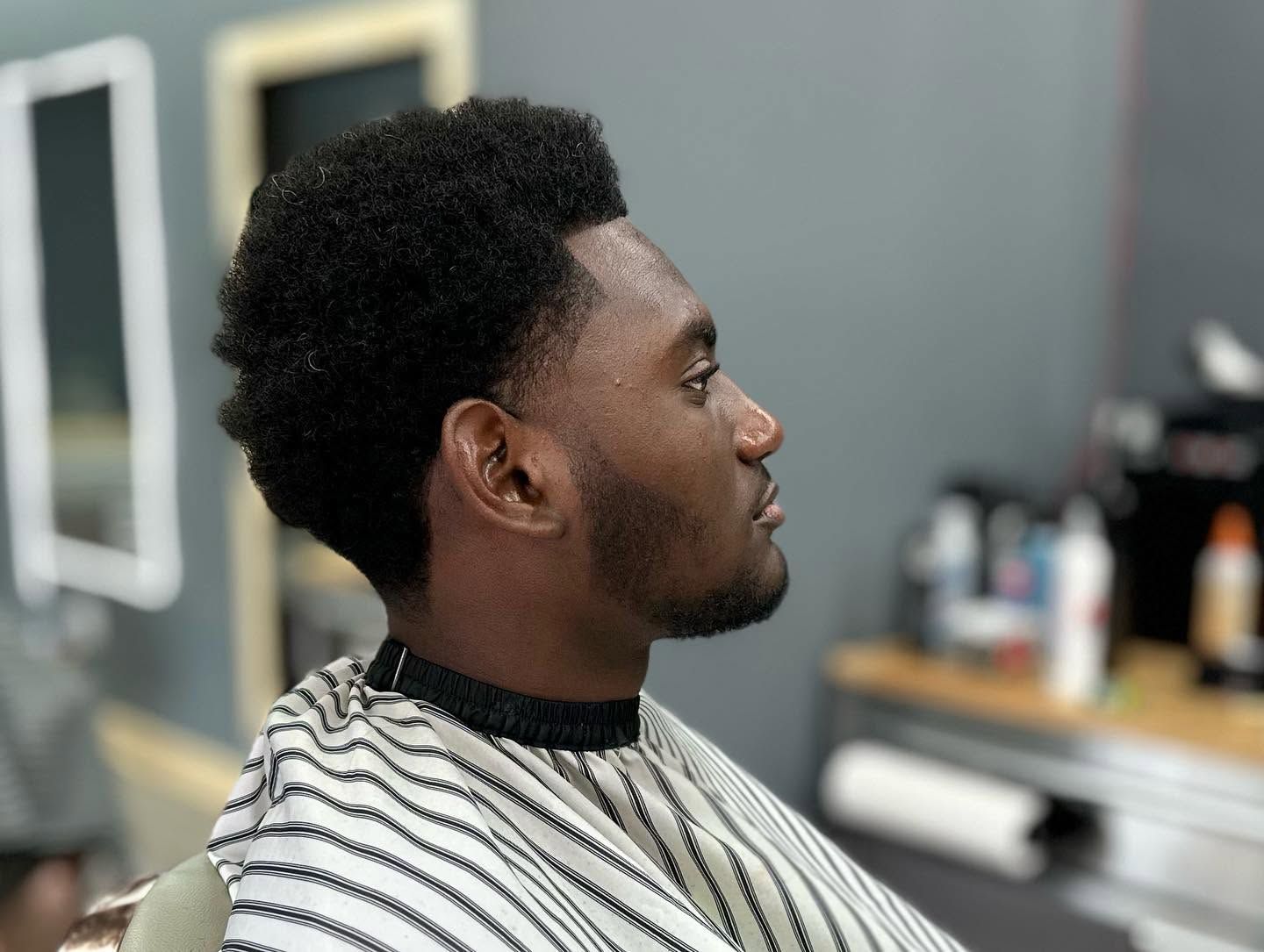 Profile view of a person in a barber chair with a striped cape, getting a haircut