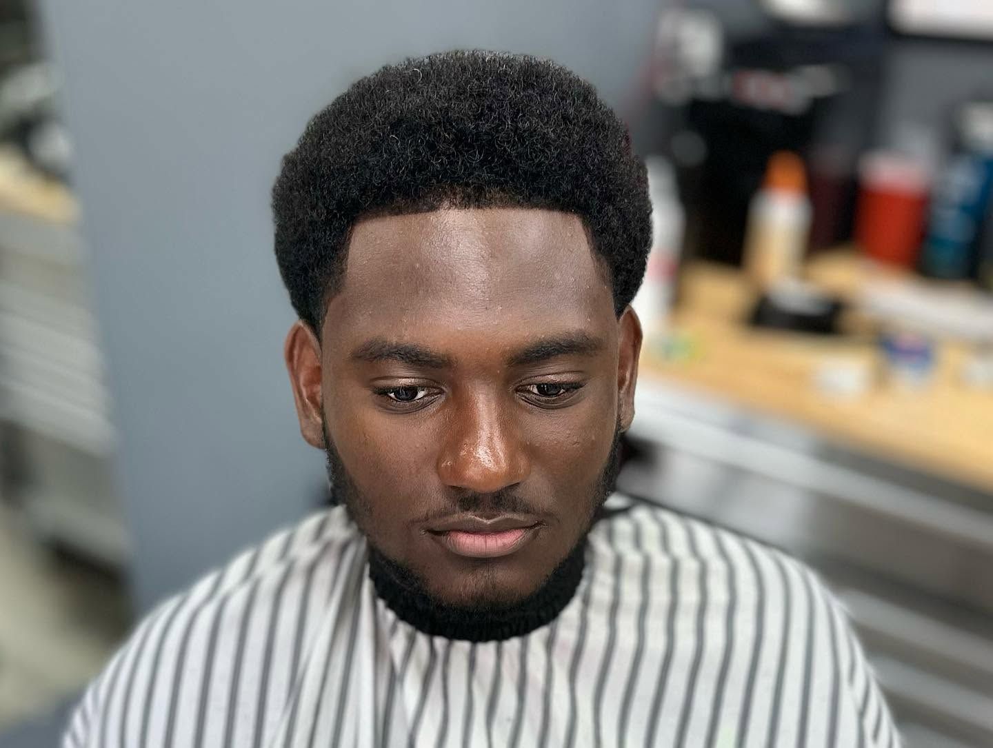 Man with trimmed beard in striped barber cape, looking down in a barbershop