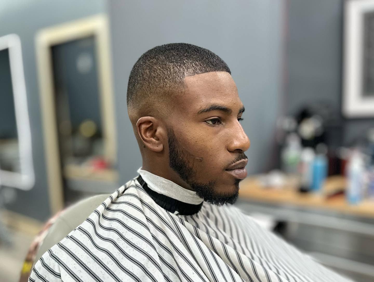 Man getting a close fade haircut in a barbershop, wearing a striped cape
