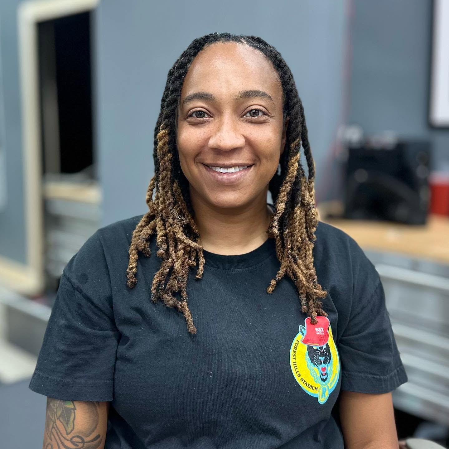 Smiling person in a black shirt with a colorful patch, standing indoors in an office setting