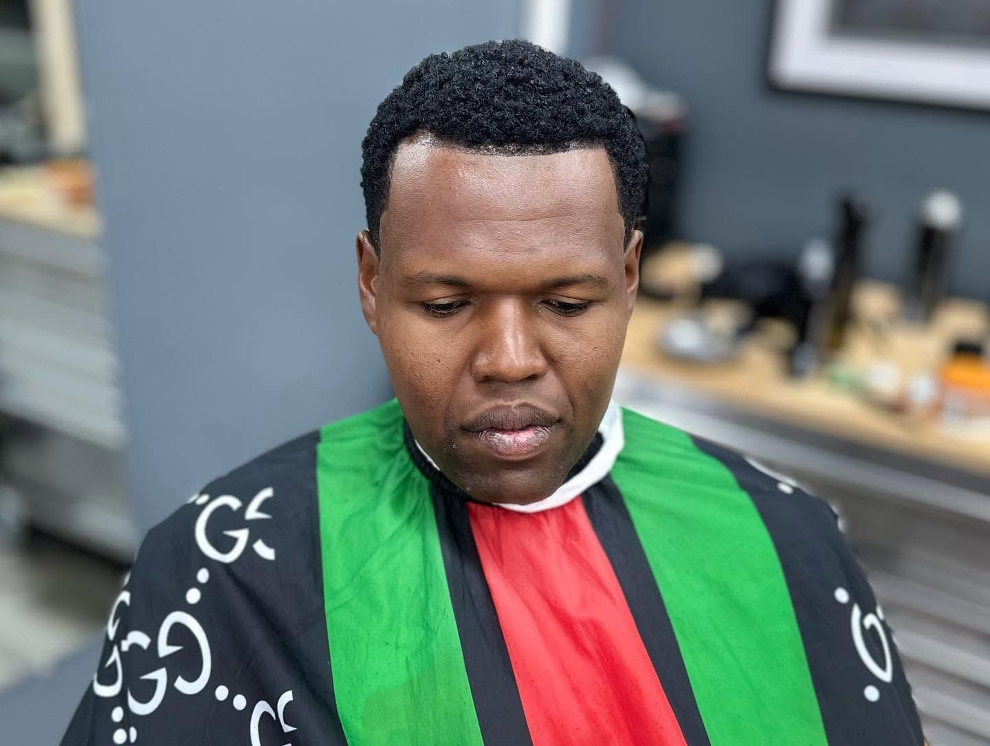 Person with short curly hair wearing a green, red, and black garment, looking downward indoors.