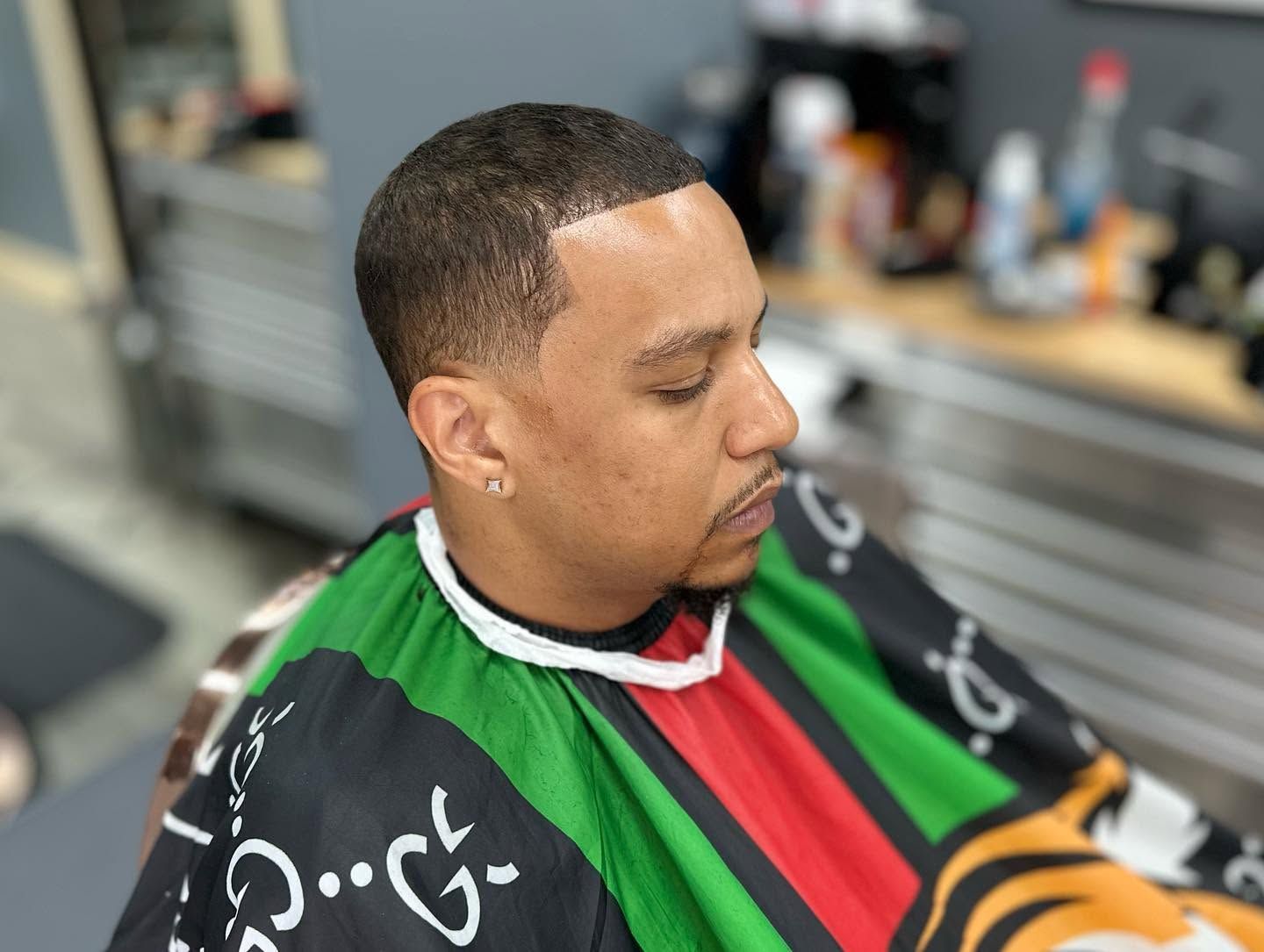 Person in a barber chair wearing a green, red, and black cape, getting a haircut.