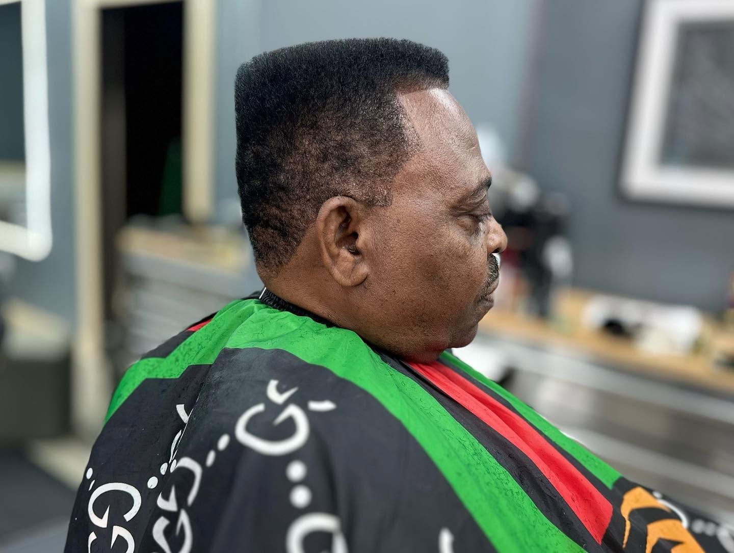 Man in green and black jacket seen in profile inside a barbershop or salon