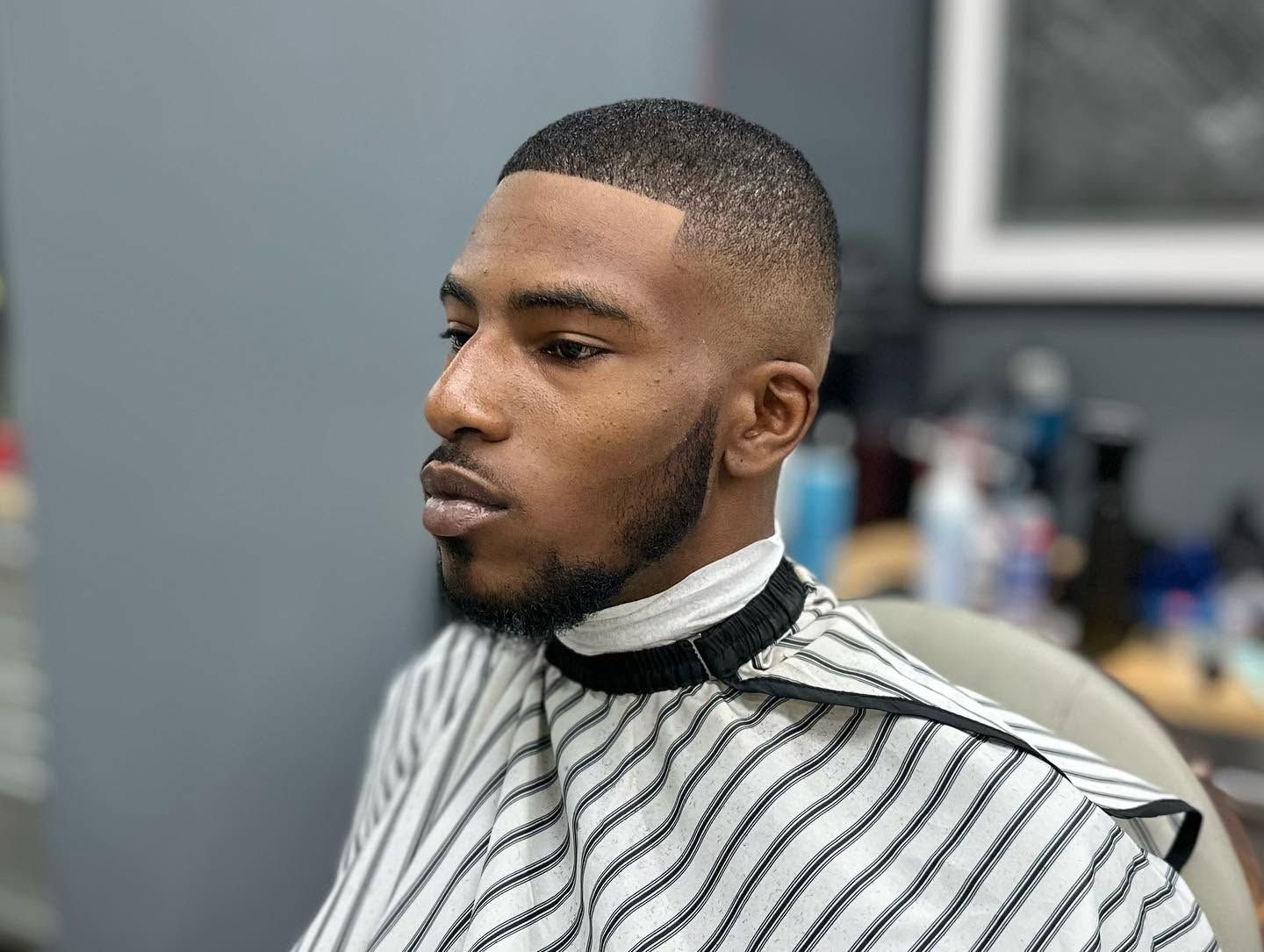Man getting a fresh haircut in a barber chair, wearing a striped cape