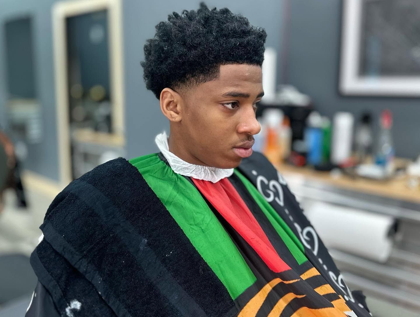 Person in a barbershop cape with green and red stripes, sitting in a chair with a fresh haircut.