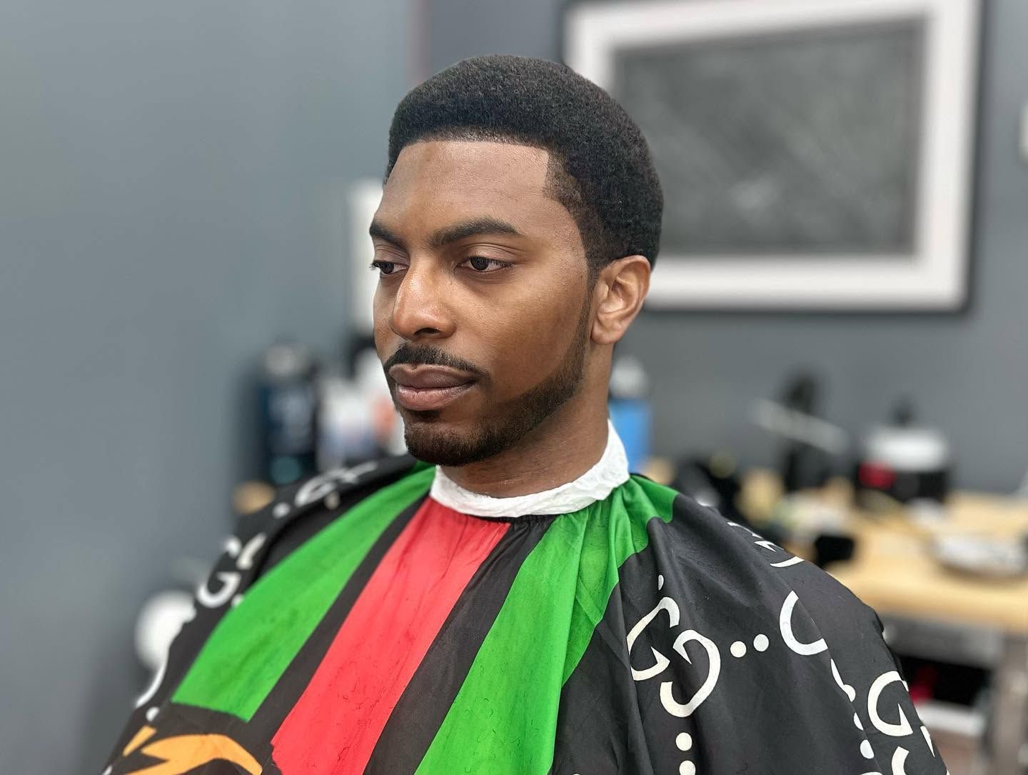 Man in a barber cape sitting in a salon chair, wearing a red and green striped cape.