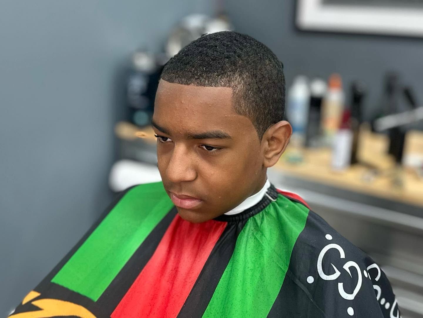 Person in a barber chair wearing a green-and-black cape, looking down during a haircut.