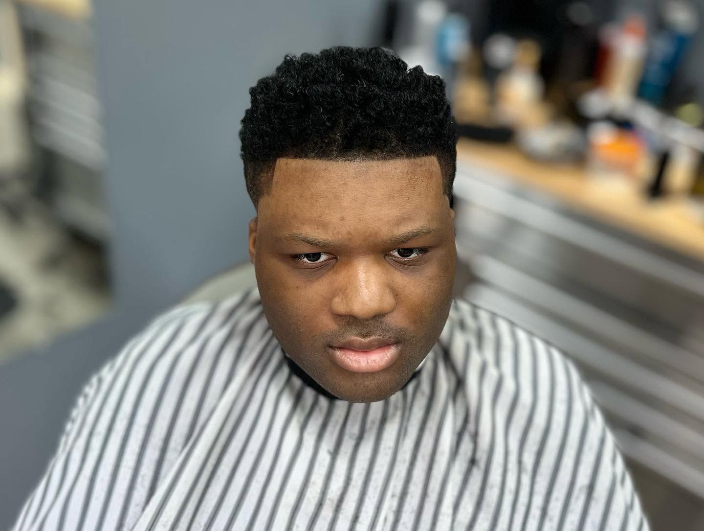 Person with short curly hair and striped cape in a barber chair, looking down in a salon.