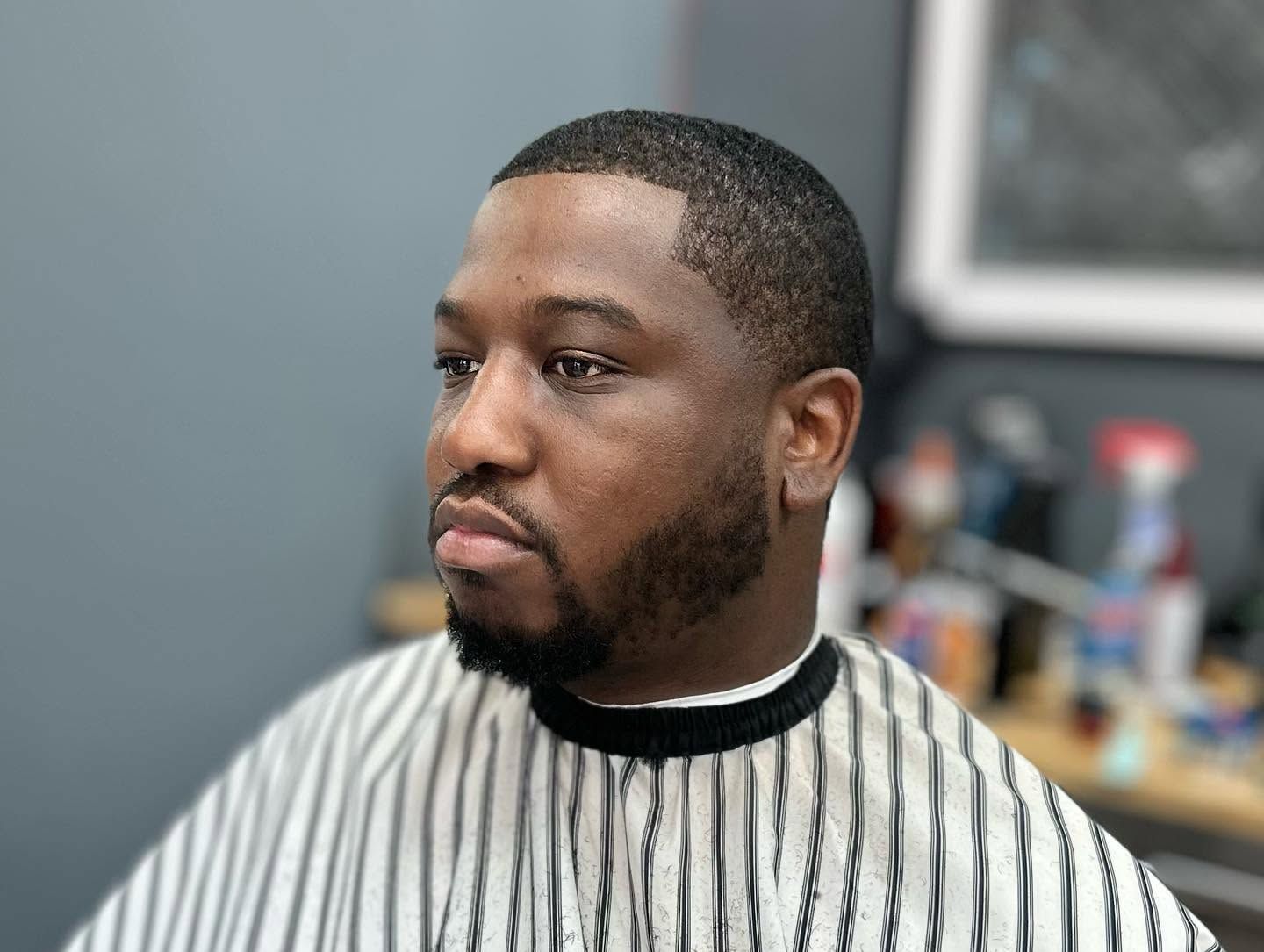Portrait of a man in a striped barber cape, seated indoors with a neutral expression.