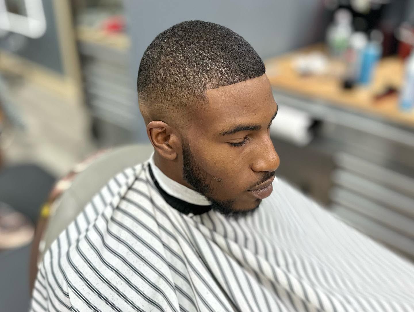 Man getting a close fade haircut in a barber chair, wearing a striped cape.