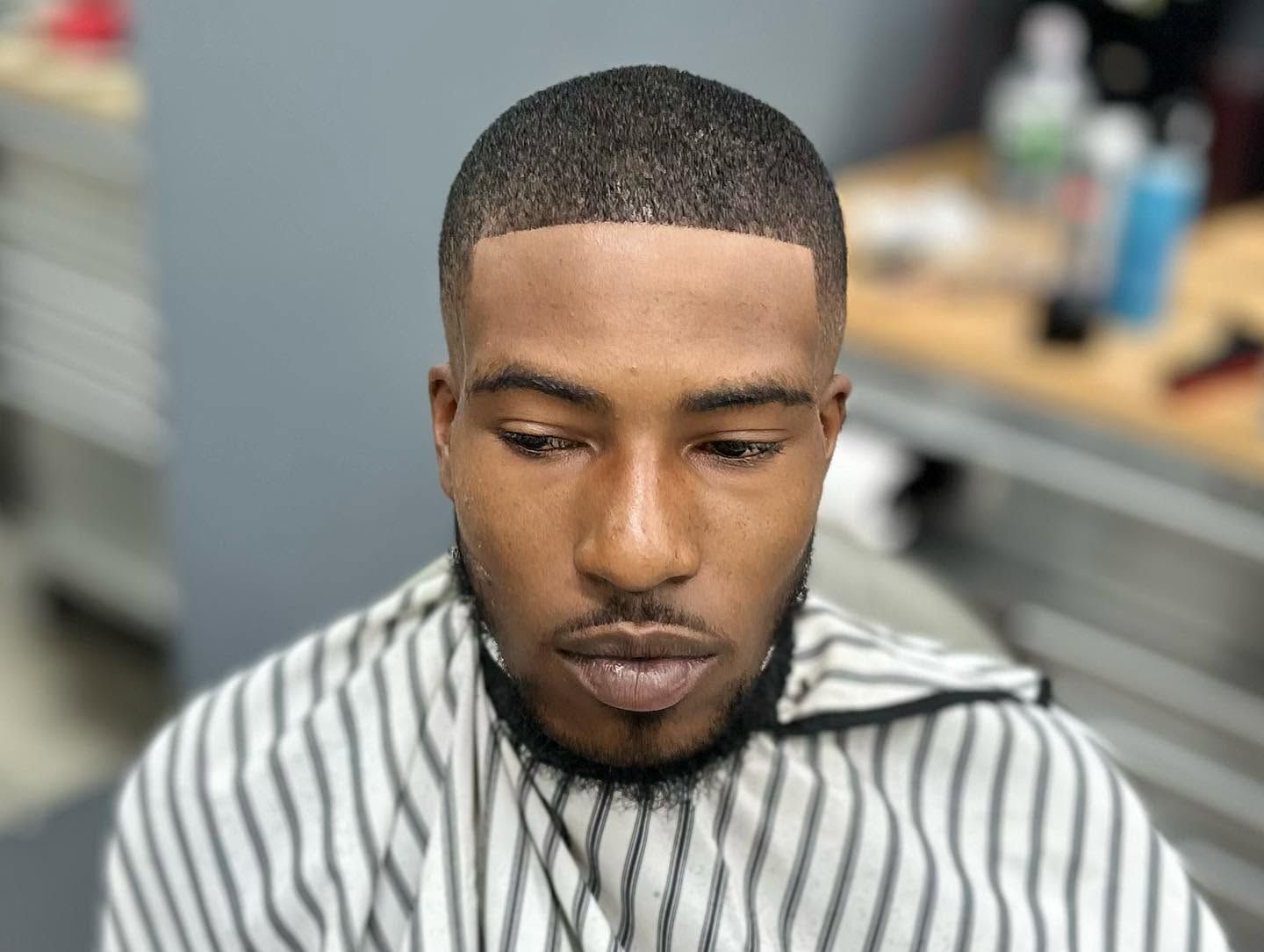Man getting a sharp haircut in a barbershop, wearing a striped cape, looking downward