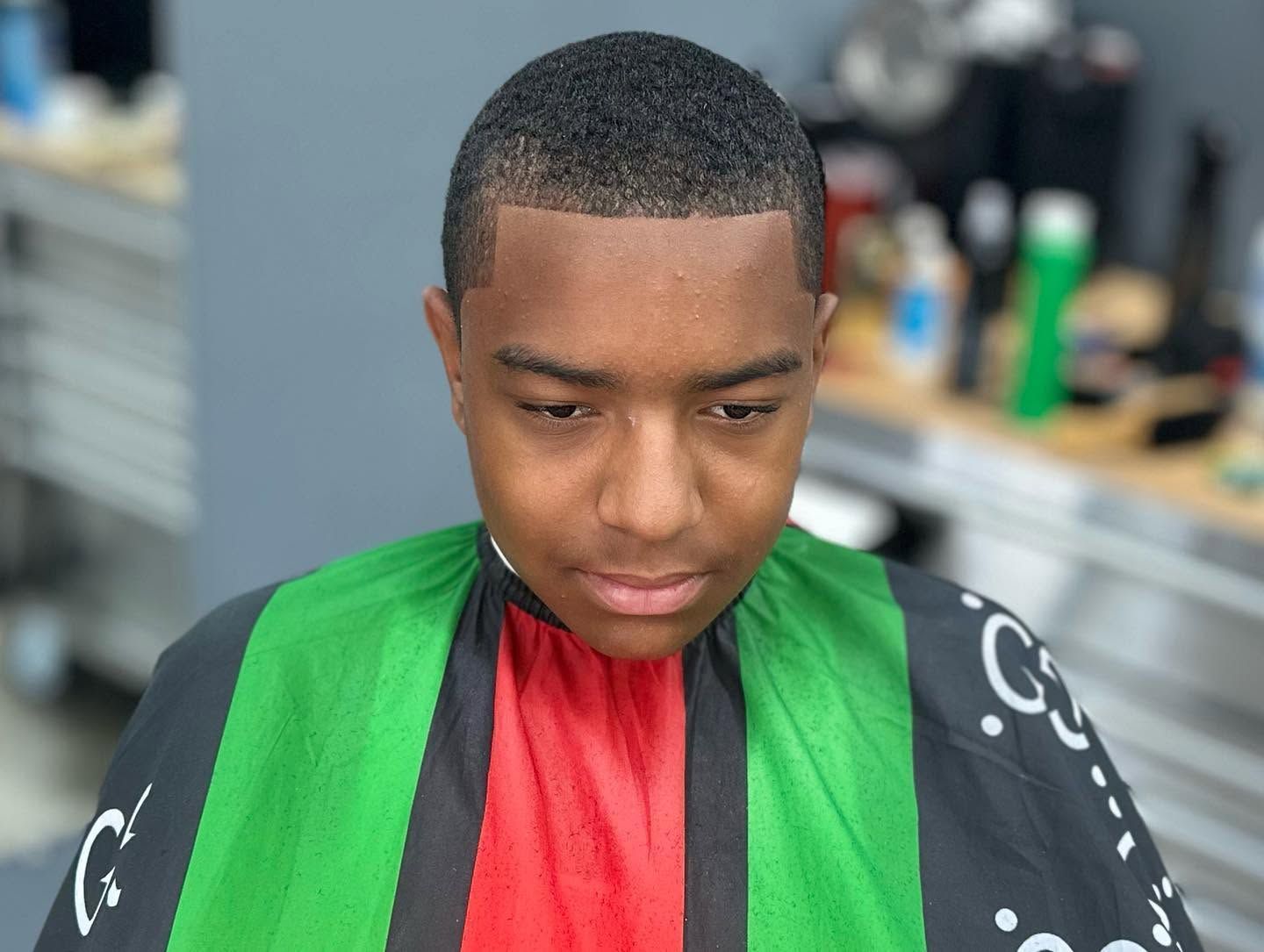 Person in a barbershop cape with red center and green-and-black sides, looking down during a haircut
