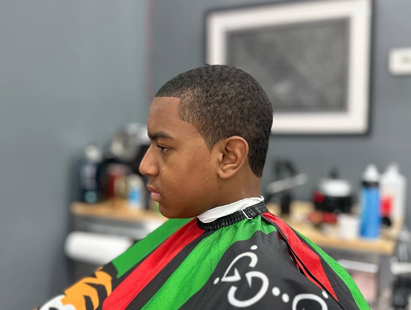 Person wearing a colorful barber cape, seated in a barbershop during a haircut.