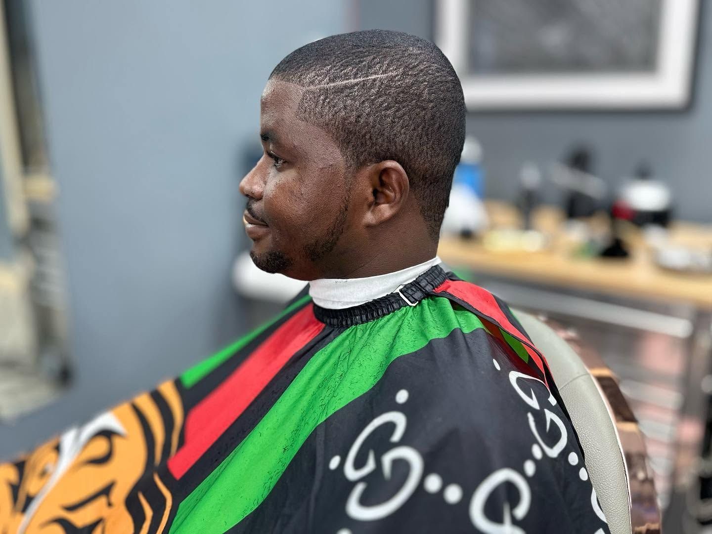 Side-profile of a man in a barber chair wearing a colorful red, green, and black haircut cape