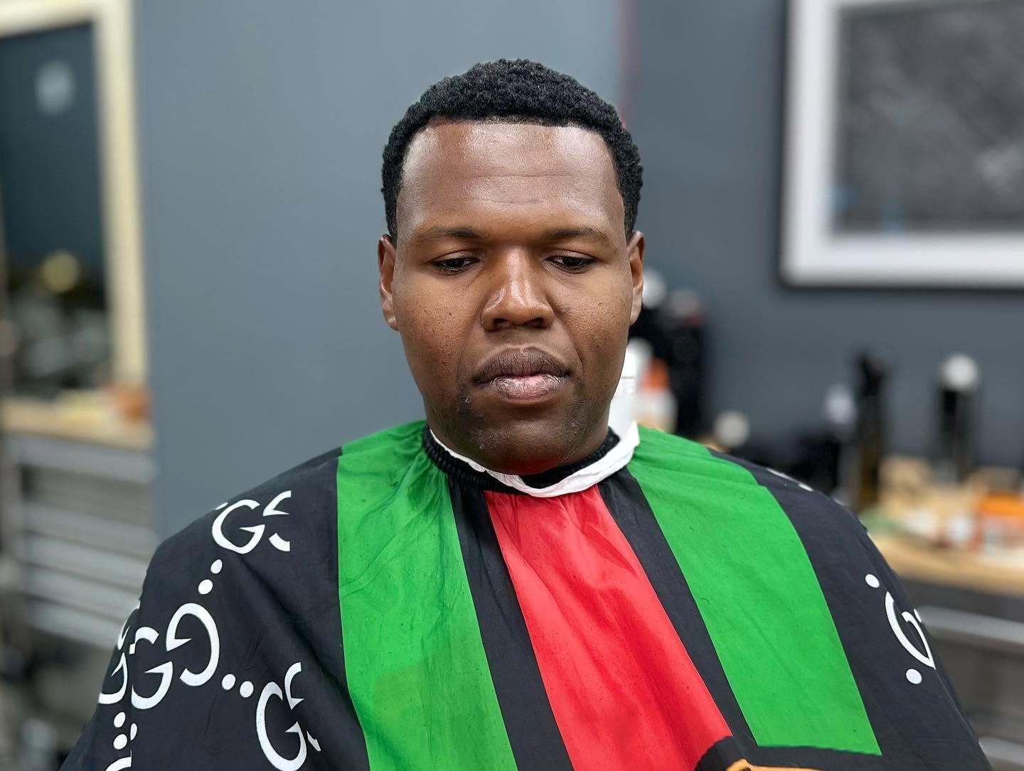 Person seated indoors wearing a black, green, and red striped garment, looking down thoughtfully.