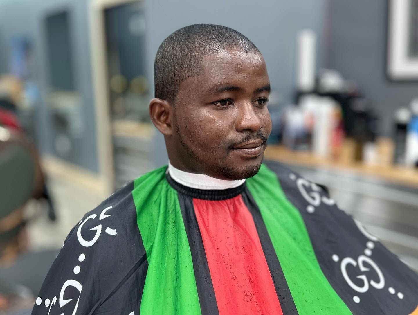 Person seated in a barber cape with green and red stripes, getting a haircut in a salon.