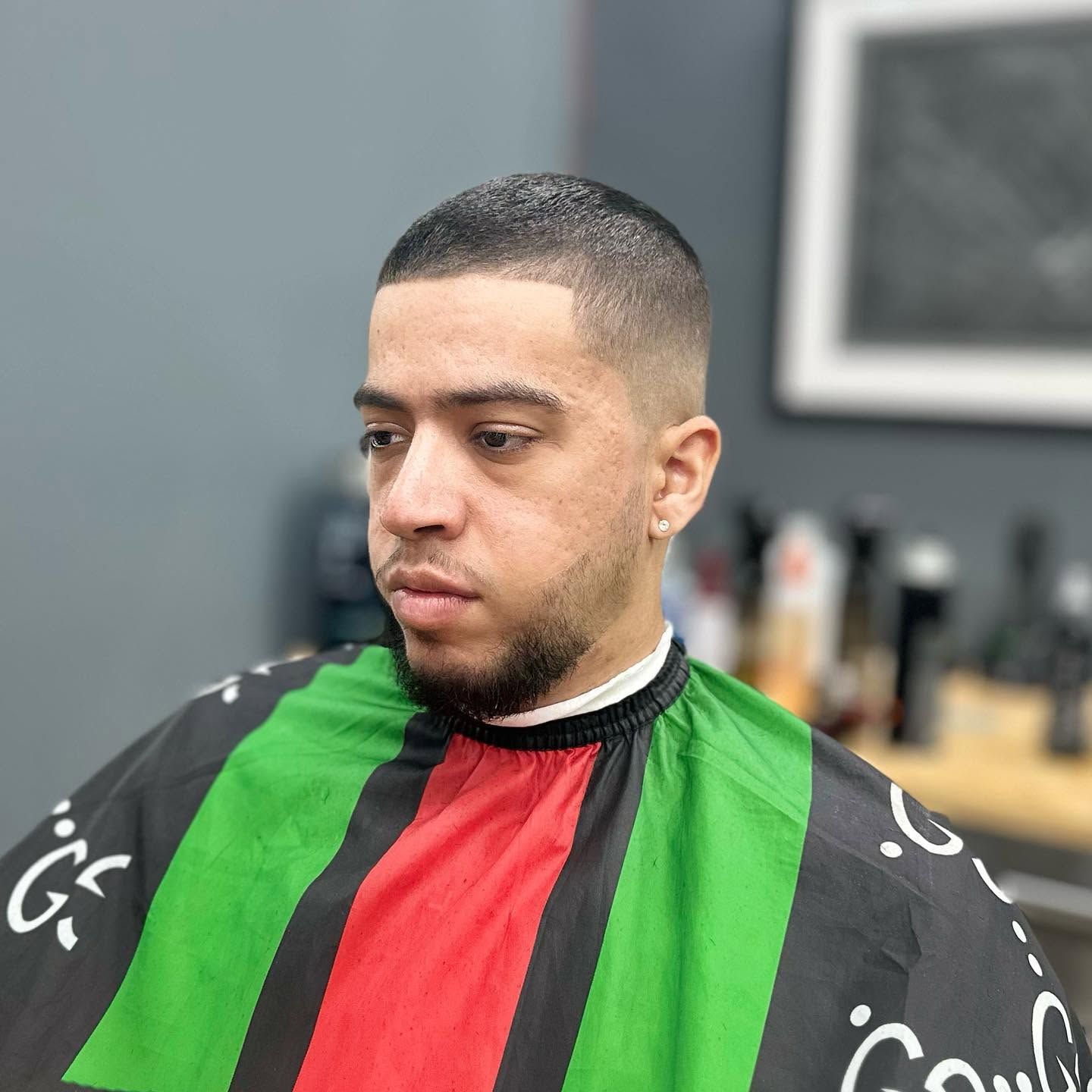 Man in a barber cape with green and red stripes, seated in a barbershop chair with a fresh short haircut.
