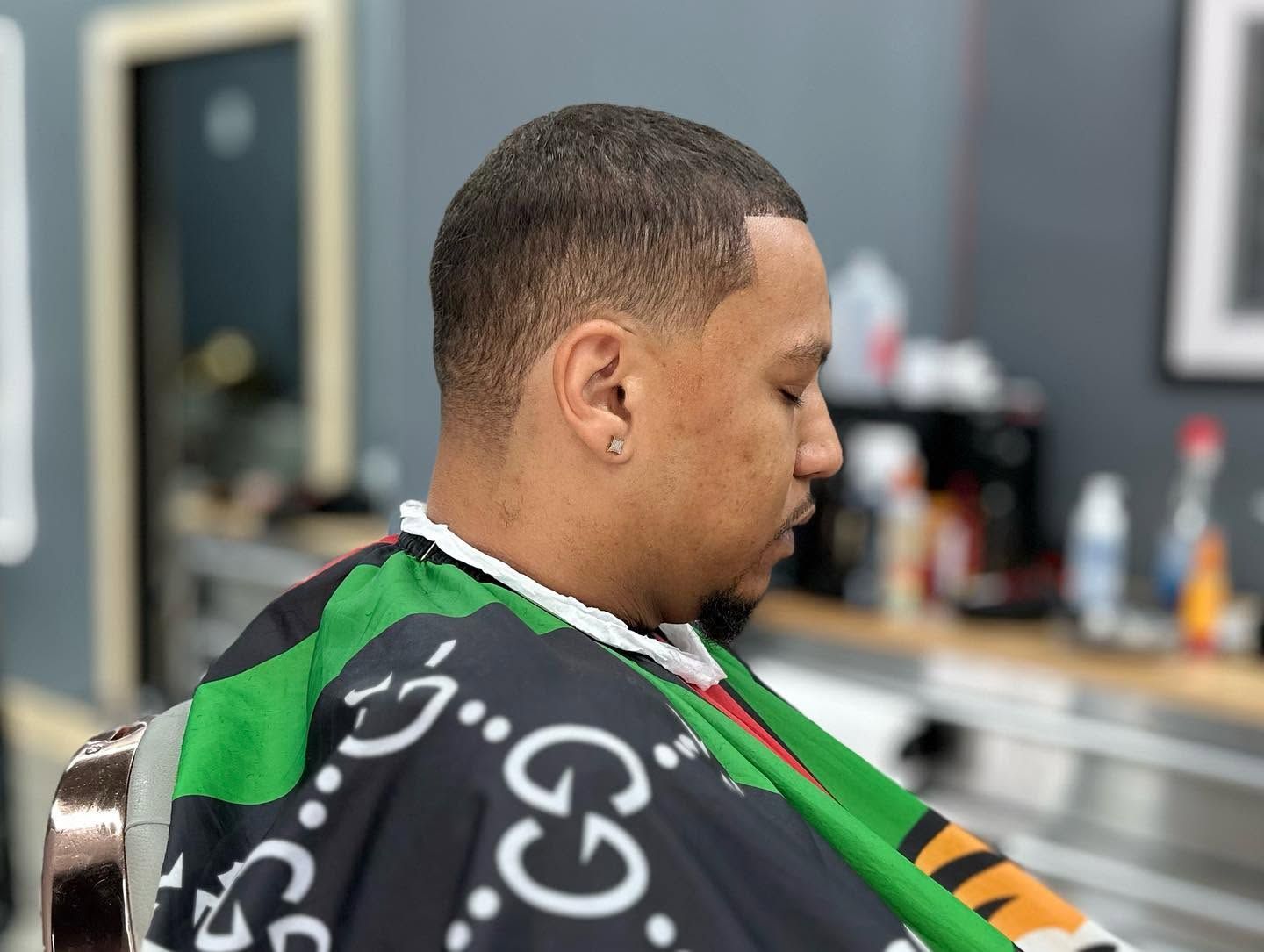 Person seated in a barbershop cape during a haircut, seen in profile.