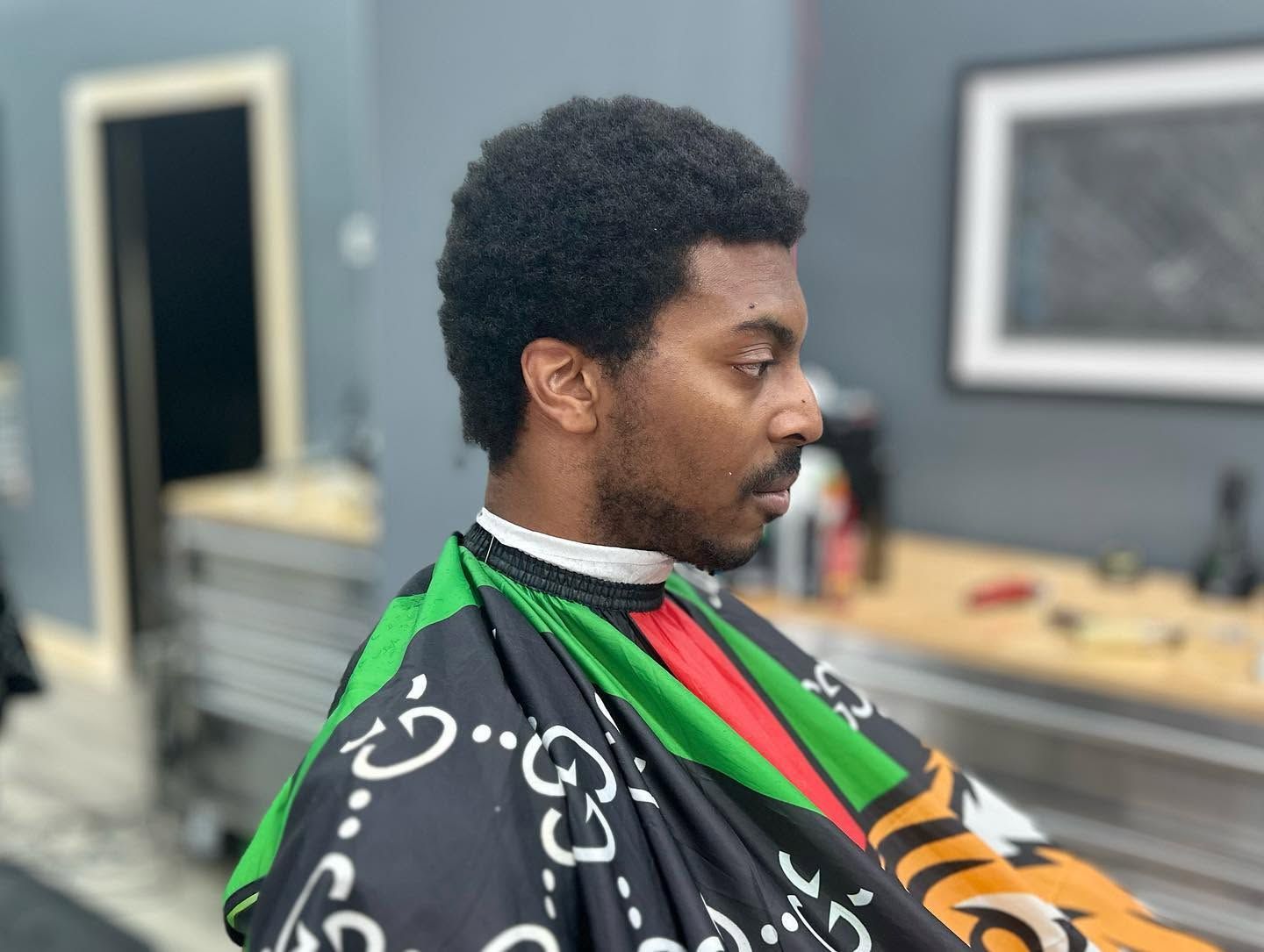 Person seated in a barbershop cape, shown in profile during a haircut.
