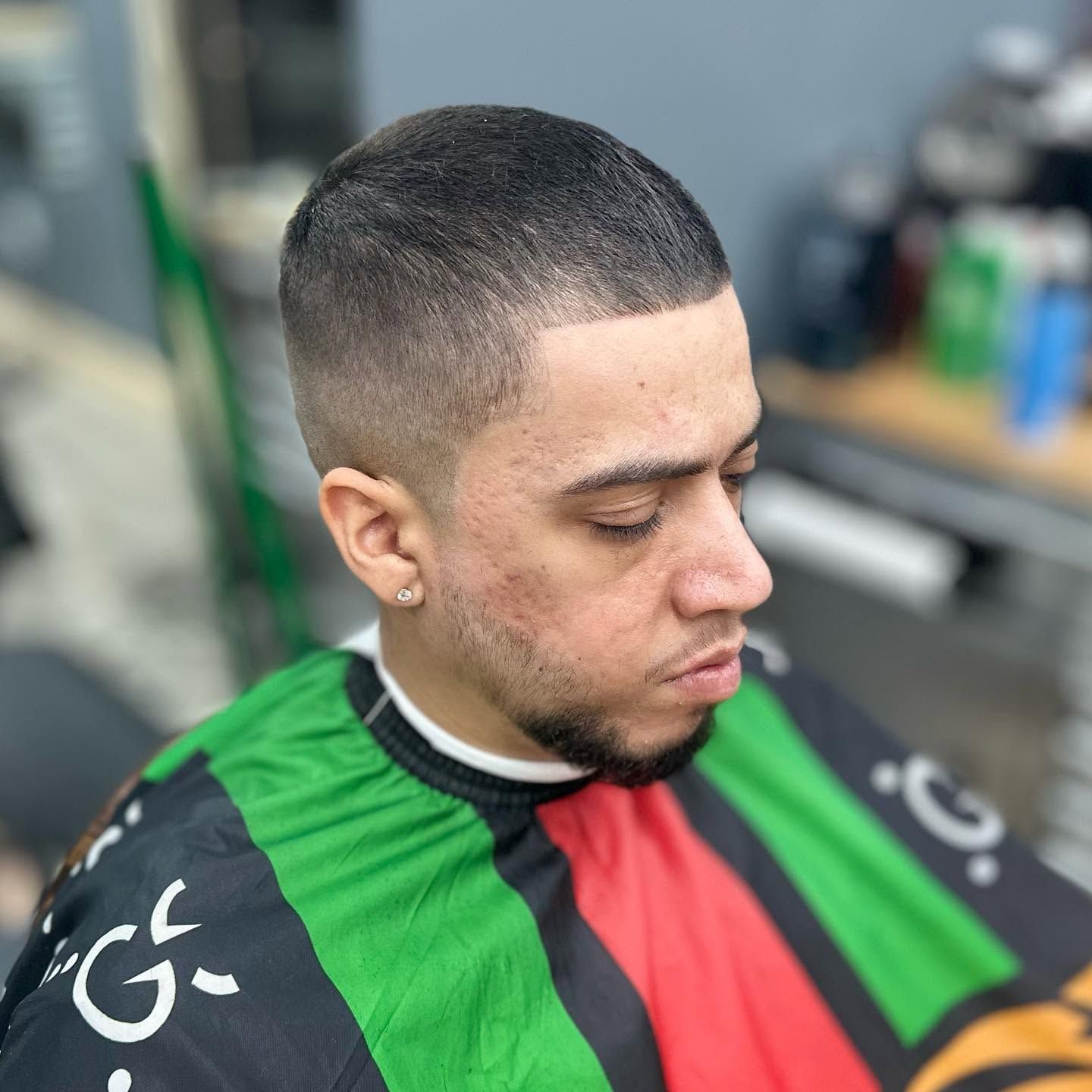 Barber cape in green, red, and black on a person seated in a barbershop, looking down.