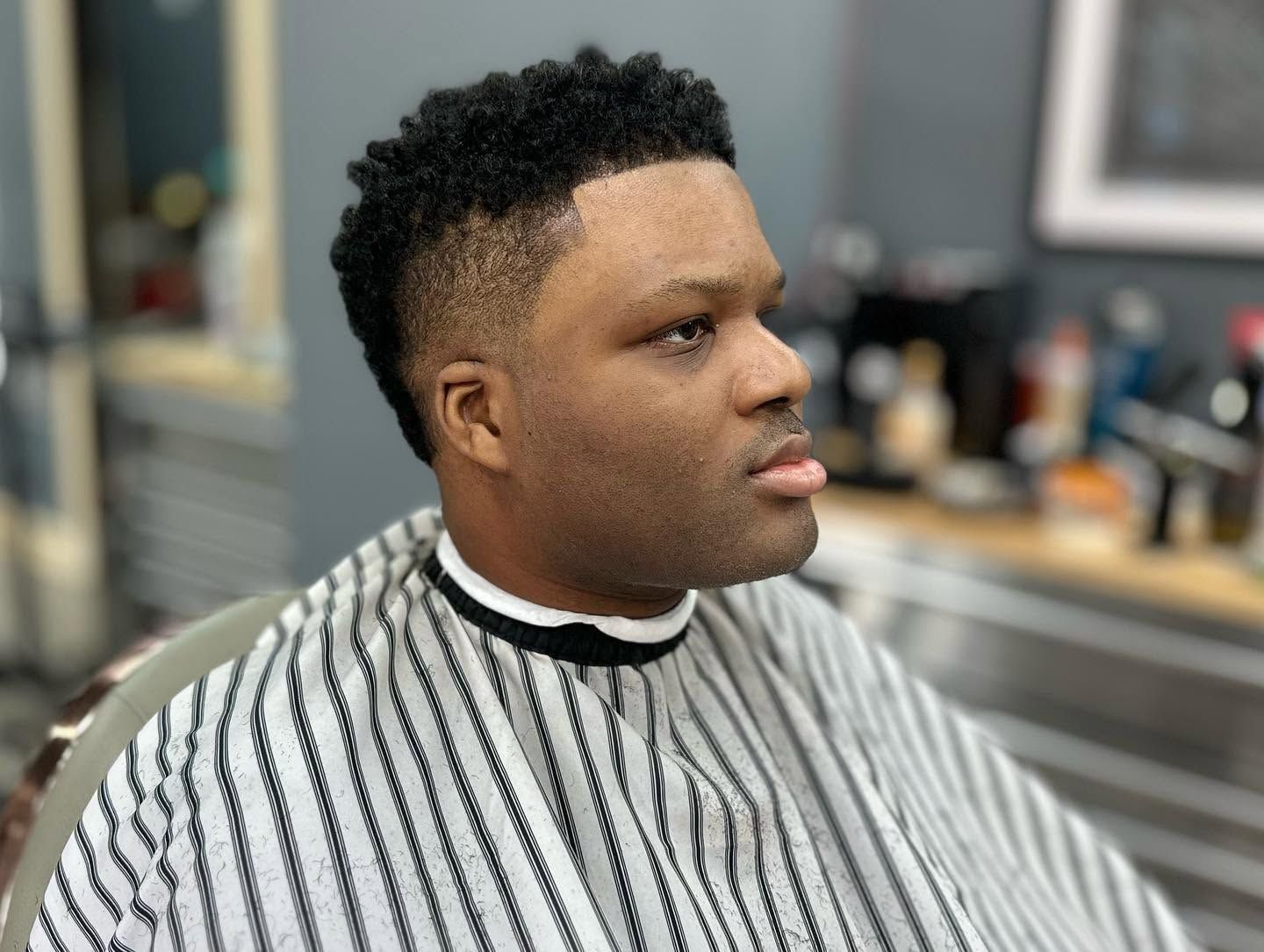 Man in striped barber cape seated in a salon chair, facing right, with a fresh fade haircut.