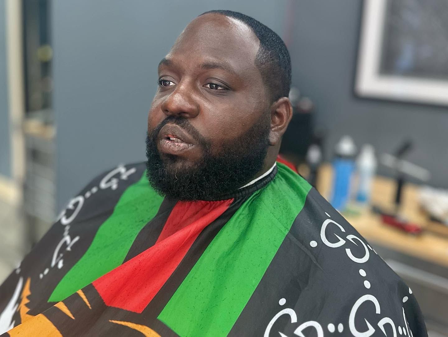 Portrait of a man in a colorful striped barber cape, seated indoors and looking to the side