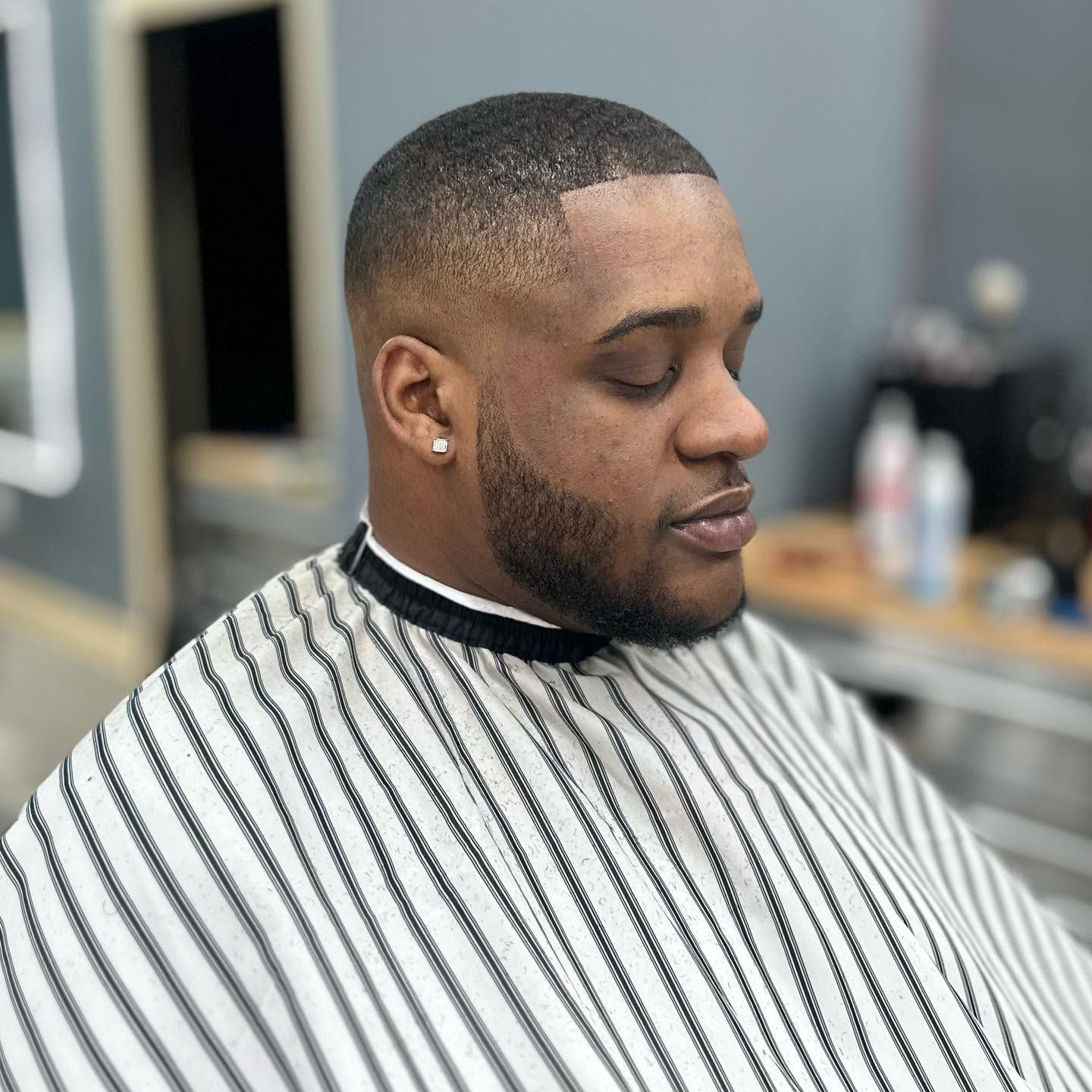 Man getting a fresh haircut in a barber chair, wearing a striped cape