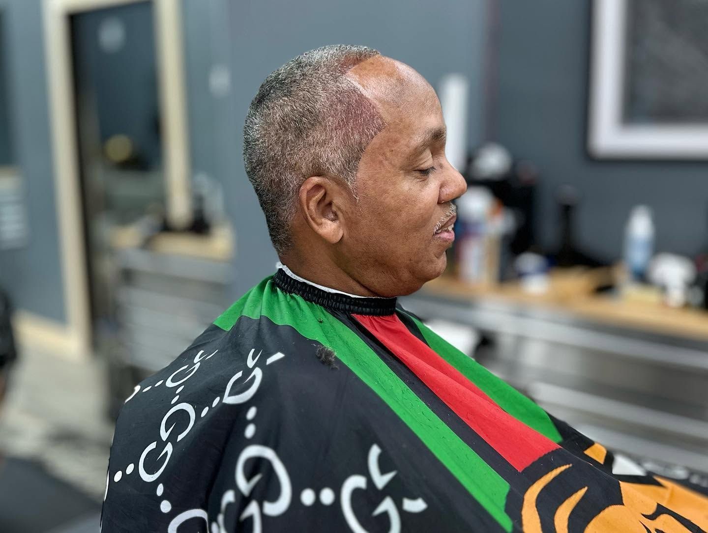 Person sitting in a salon chair with a black, green, and red cape draped over their shoulders