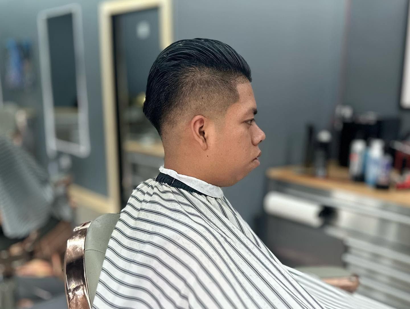 Person getting a haircut in a barbershop, seated in a striped cape near mirrors and styling tools.