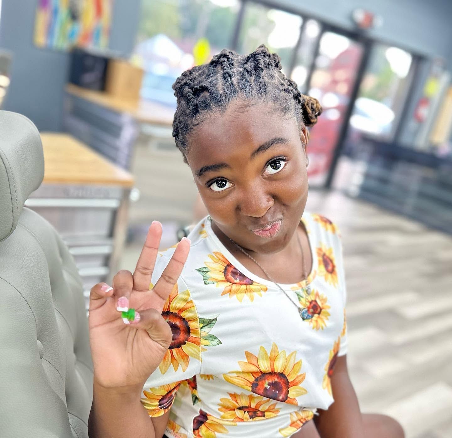 Smiling child in sunflower shirt making a peace sign while sitting indoors