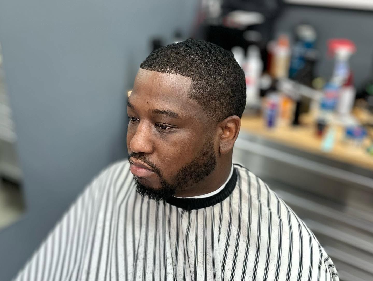 Man with short beard in a striped barber cape, looking to the side in a salon chair.