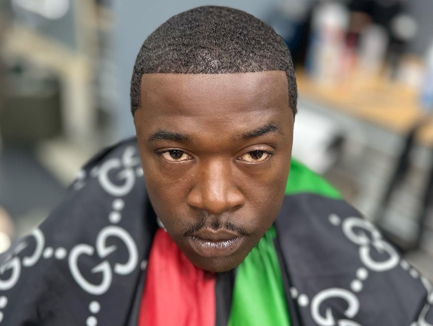 Close-up of a man wearing a black patterned jacket and red shirt, looking directly at the camera.