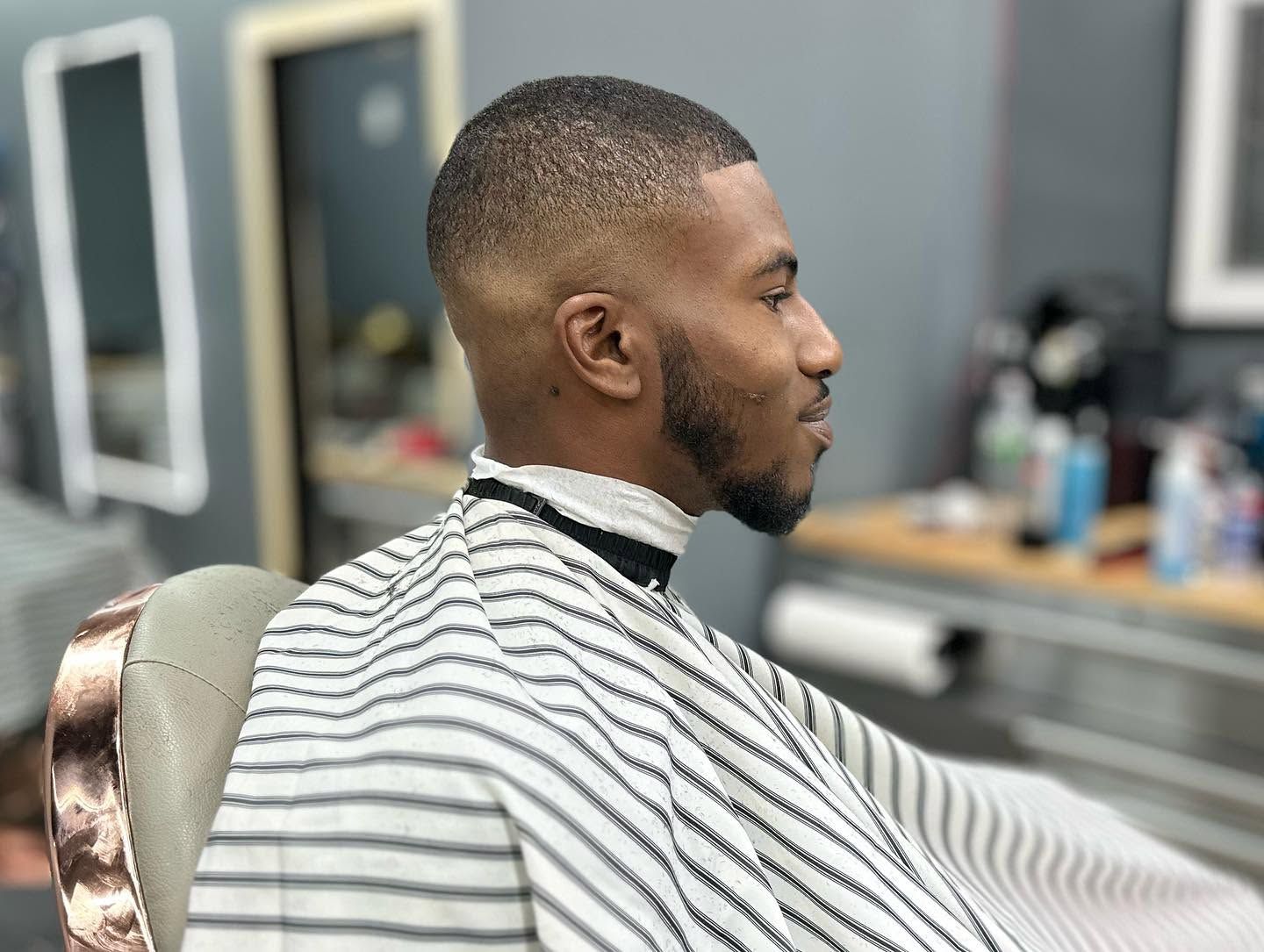 Man in striped barber cape seated in a salon chair, side profile with a fresh fade haircut.