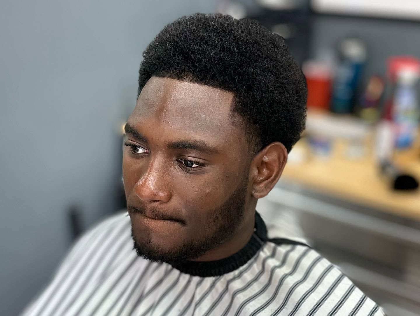 Man sitting in a barber chair with a striped cape, looking down thoughtfully in a barbershop