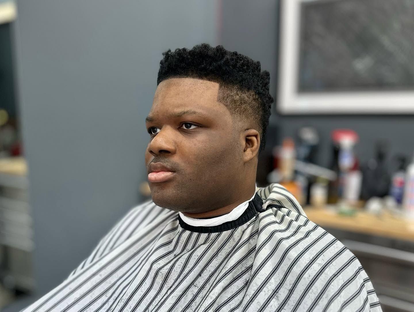 Person in a black-and-white striped barber cape, seated in a salon chair with a neutral expression.