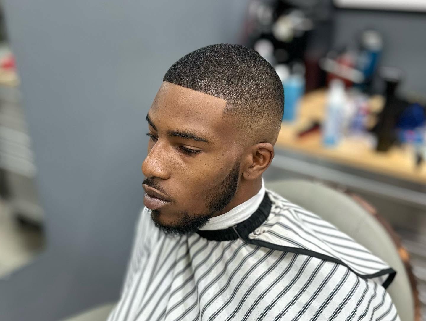 Man in striped barber cape with a fresh fade haircut in a barbershop chair