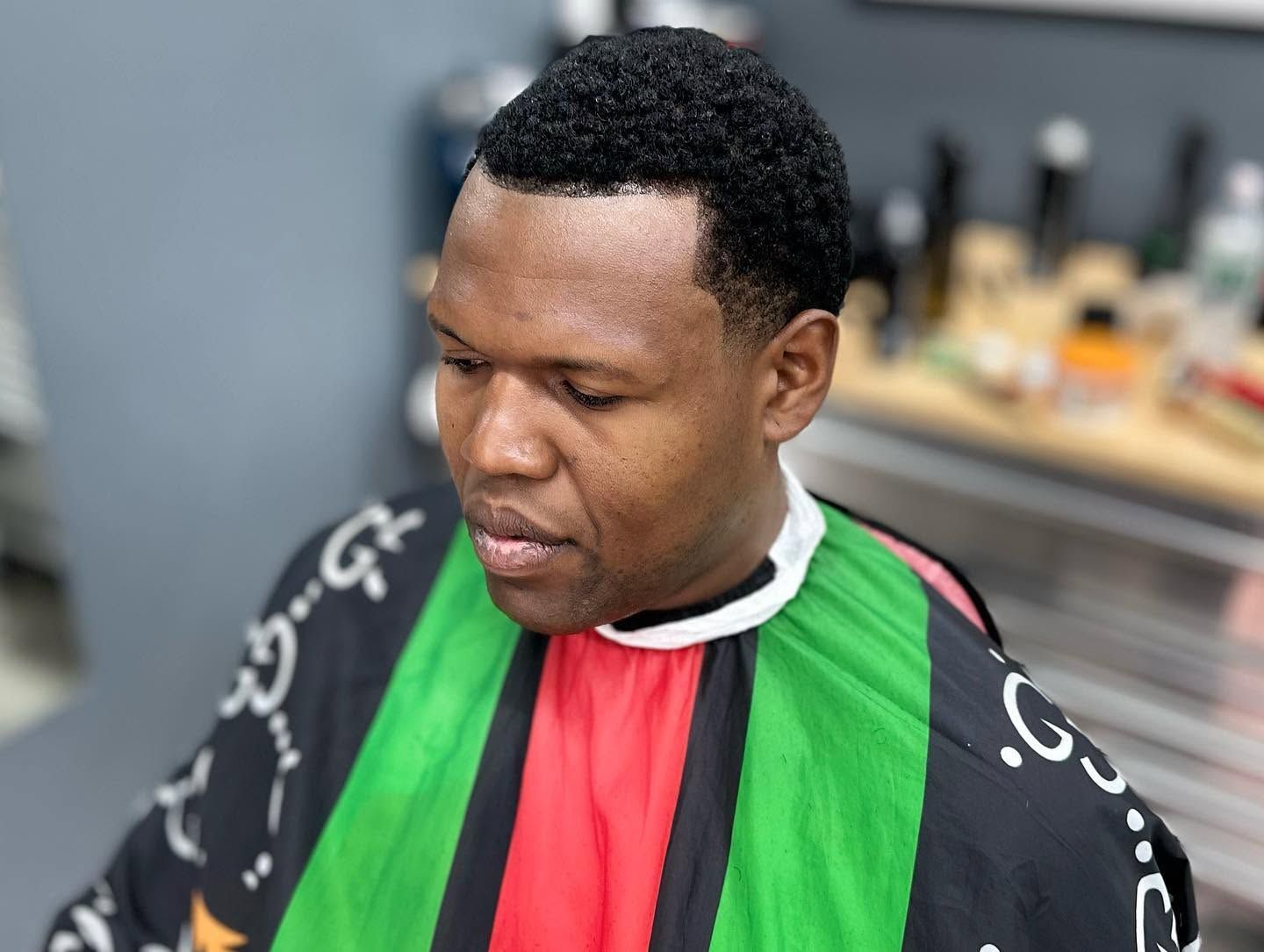 Person wearing a red, green, and black cape-like garment, looking down indoors.