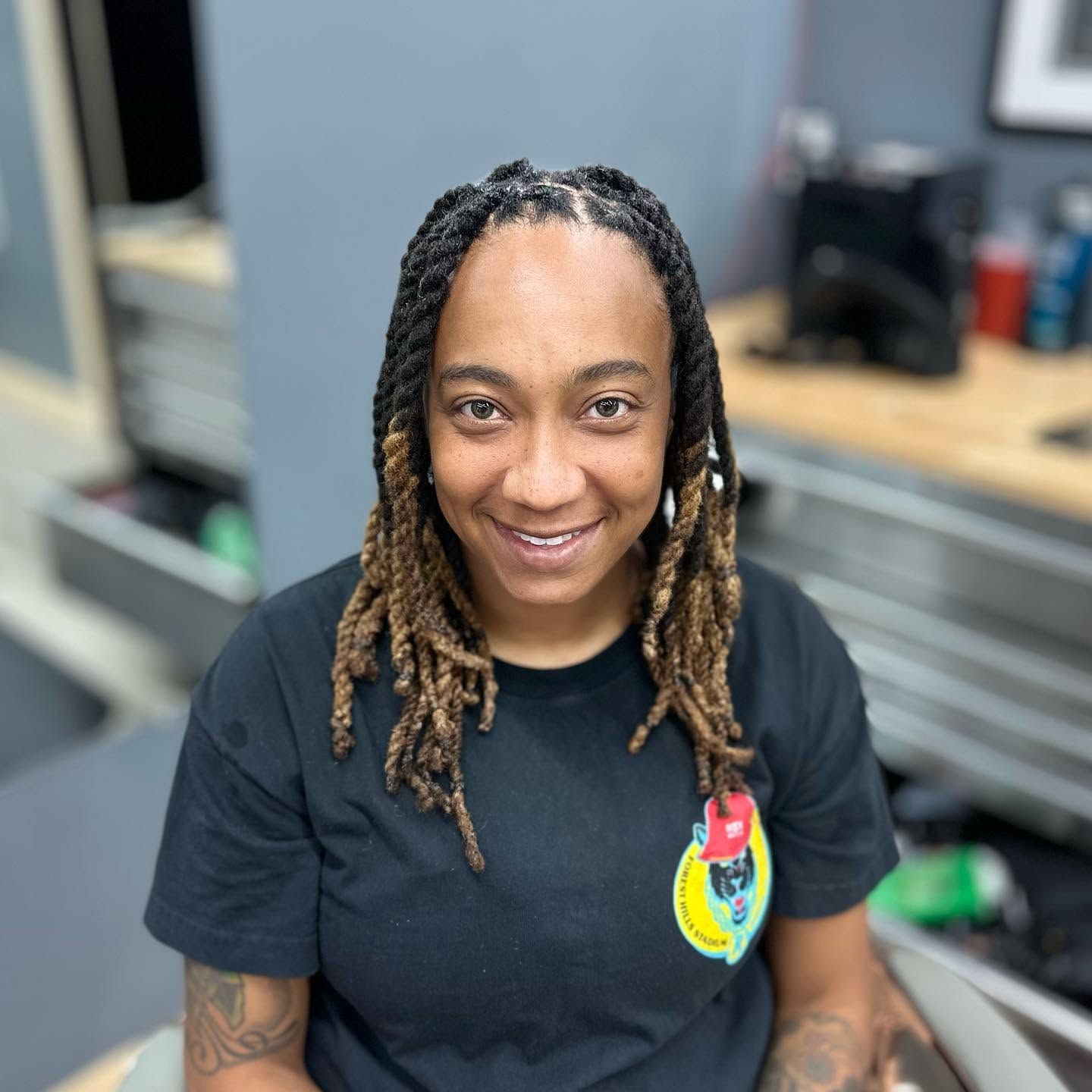 Smiling person with braided hair in a black T-shirt, seated in an office setting